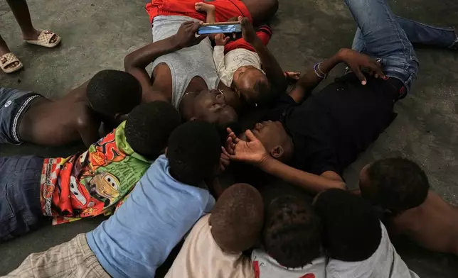 Children watch a movie on a mobile phone at a shelter for families displaced by gang violence in Port-au-Prince., Haiti, Friday, July 31, 2026. (AP Photo/Odelyn Joseph)