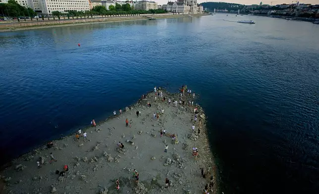 People walk on a sandbar underneath the Danube's Margareth Bridge in downtown Budapest, Hungary, Wednesday Aug. 5, 2026, as the river, which runs through 10 European countries, has receded never-before-seen low water levels. (AP Photo/Bela Szandelszky)