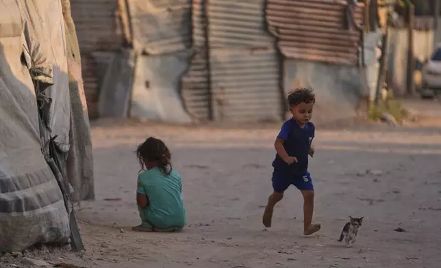 Majed Tafesh, 3, runs after his cat while playing among the tents at a camp for displaced Palestinians in Deir al-Balah, central Gaza Strip, Thursday, Aug. 6, 2026. (AP Photo/Abdel Kareem Hana)