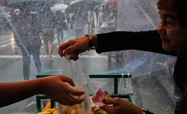 Vendor Elsie Andol sells bananas during rain due to the Southwest Monsoon enhanced by Tropical Storm Kujira on Wednesday, Aug. 5, 2026, in Quezon city, Metro Manila, Philippines. (AP Photo/Aaron Favila)