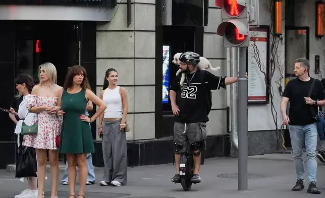 A man with a dog perched on his shoulder balances on an electric unicycle at a street crossing in Moscow, Tuesday, Aug. 4, 2026. (AP Photo/Pavel Bednyakov)