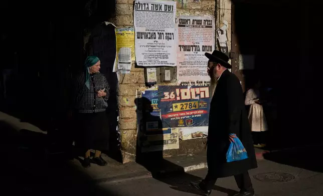 Ultra-Orthodox Jews walks past pashkevilim, posters used to publicize news and important messages in the ultra-Orthodox community, in the Mea Shearim neighborhood of Jerusalem, Wednesday, July 8, 2026. (AP Photo/Ohad Zwigenberg)
