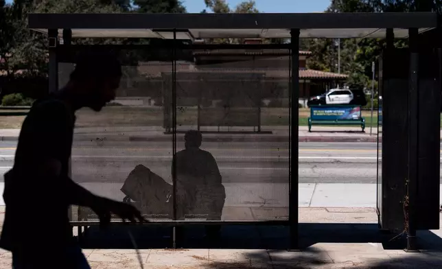 A person sits in the shade at a bus stop in Los Angeles, Friday, July 31, 2026. (AP Photo/Jae C. Hong)