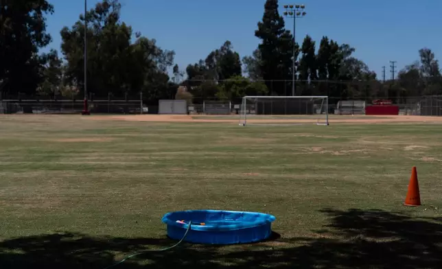 A small plastic pool is filled with water for children to cool off on a soccer field in Los Angeles, Friday, July 31, 2026. (AP Photo/Jae C. Hong)