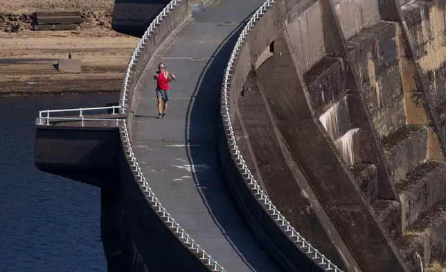 A member of the public crosses a reservoir wall at Baitings reservoir near Sowerby Bridge as water levels drop throughout the country, in Sowerby Bridge, England, Thursday, Aug. 13, 2026. (AP Photo/Jon Super)