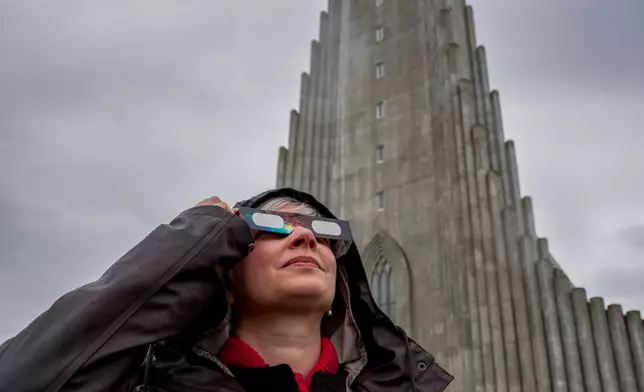 Anita Sauckel, an employee of the university of Iceland uses solar eclipse glasses to look up at the sun in front of the Hallgrímskirkja church ahead of a solar eclipse in Reykjavik, Iceland, Wednesday, Aug. 12, 2026. (AP Photo/Marco di Marco)