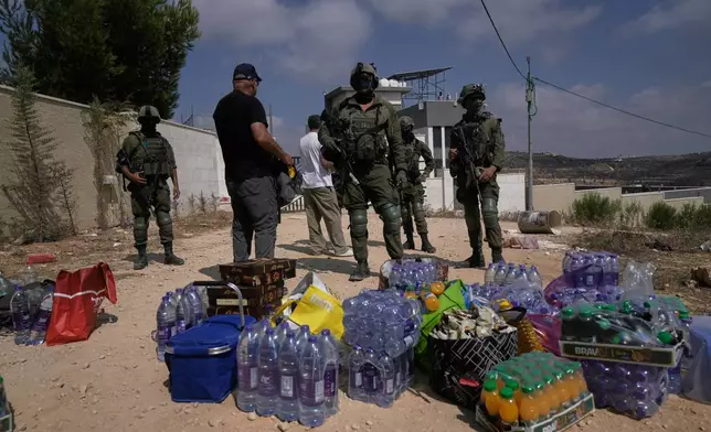 Activists accumulate food and water supplies in front of Israeli army soldiers who are blocking the road leading to the houses of three Palestinian families that have been besieged by Israeli settlers for six days, in the occupied West Bank village of Qusra, south of Nablus, Friday, Aug. 14, 2026. (AP Photo/Majdi Mohammed)