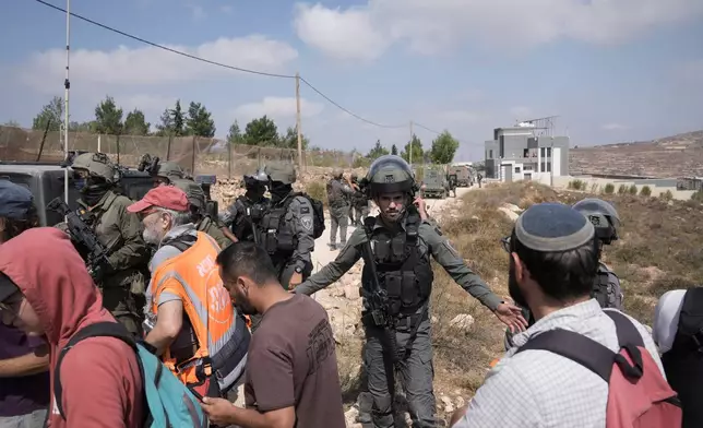 Israeli army soldiers turn back activists who marched with food and water supplies toward the houses of three Palestinian families that have been besieged by Israeli settlers for six days, in the occupied West Bank village of Qusra, south of Nablus, Friday, Aug. 14, 2026. (AP Photo/Majdi Mohammed)