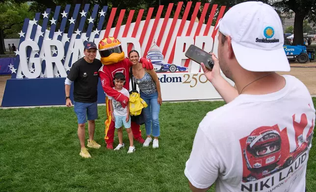 David Avalos, 7, and his parents Hector Avalos and Ana Oceguda, of Washington, take a photo with the mascot for Firestone Tires during events prior to Sunday's Freedom 250 Grand Prix auto race in Washington, Saturday, Aug. 22, 2026. (AP Photo/Jacquelyn Martin)