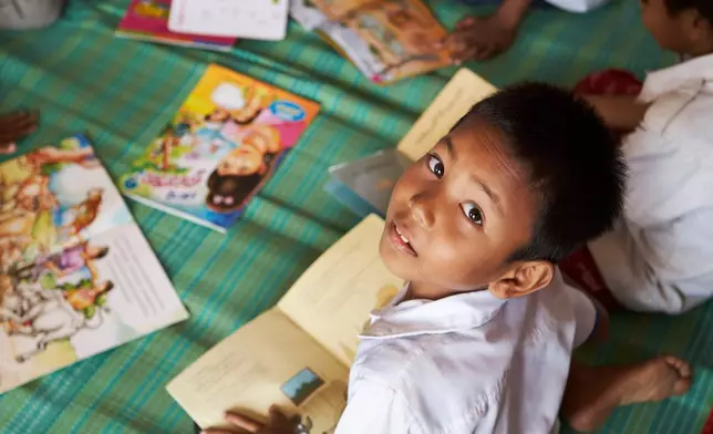 A student looks up from his picture book at a school in one of the floating villages of Cambodia's Tonle Sap Lake on Monday, June 29, 2026. (AP Photo/Aniruddha Ghosal)