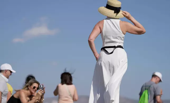 A tourist wearing a hat poses for a photograph on the rocky Areios Pagos Hill next to the Acropolis in Athens, Greece, Friday, Aug. 14, 2026. (AP Photo/Thanassis Stavrakis)