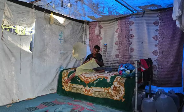Mohammed Al-Sarsak, 16, makes a kite inside the tent where he lives in Deir al-Balah, central Gaza Strip, Wednesday, Aug. 26, 2026. (AP Photo/Abdel Kareem Hana)