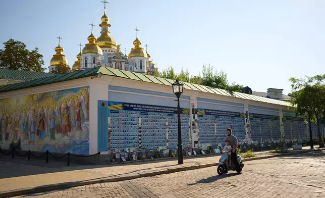 A man and a child observe a daily nationwide minute of silence in memory of soldiers killed in the war with Russia next to The Wall of Remembrance of the Fallen for Ukraine in Kyiv, Friday, Aug. 21, 2026. (AP Photo/Francisco Seco)