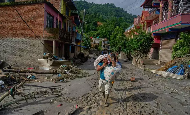 Residents carry their belongings as they walk to safer areas in the aftermath of flash floods in Devighat, in Nepal's Nuwakot district, Thursday, Aug. 27, 2026. (AP Photo/Niranjan Shrestha)