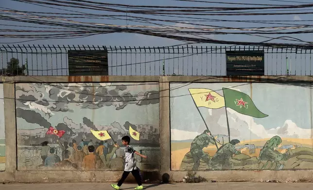 A boy walks past murals depicting Kurdish YPG and YPJ fighters battling Islamic State militants in Qamishli, northeastern Syria, Wednesday, Aug. 26, 2026. (AP Photo/Baderkhan Ahmad)