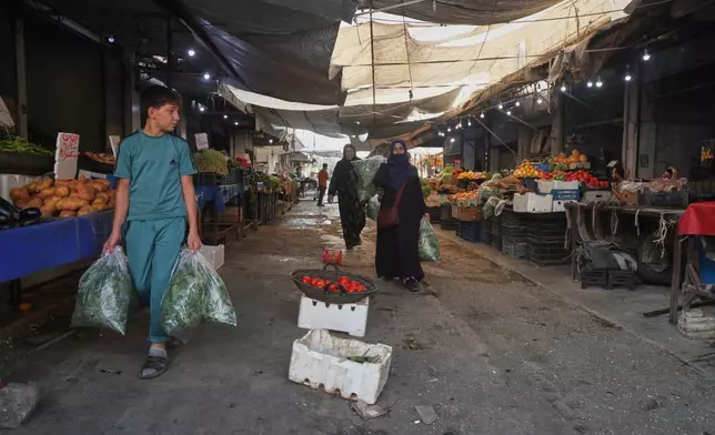 Residents carry bags of leafy greens past produce stalls at a market in Qamishli, northeastern Syria, Wednesday, Aug. 26, 2026. (AP Photo/Baderkhan Ahmad)