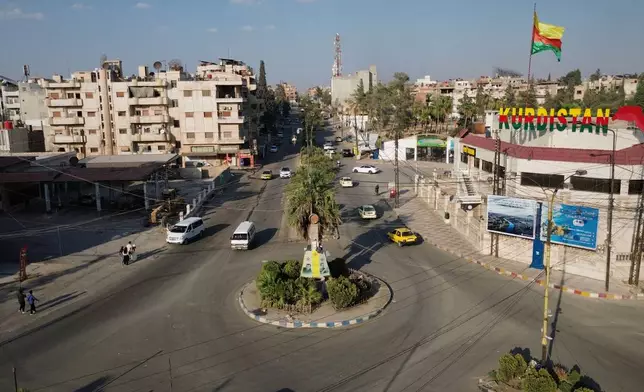 A flag bearing Kurdish colors flies above a building marked "Kurdistan" as traffic moves through an intersection in Qamishli, northeastern Syria, Wednesday, Aug. 26, 2026. (AP Photo/Baderkhan Ahmad)