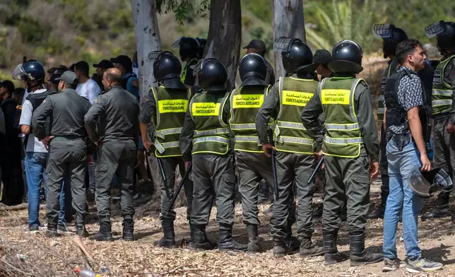 Moroccan security forces stand guard as migrants gather on a hill attempting to cross from the border town of Fnideq to the Spanish enclave of Ceuta, Saturday, Aug. 15, 2026. (AP Photo)