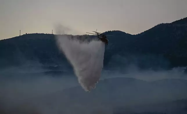 A firefighting helicopter drops water over a smoke-filled forest during a wildfire near Porto Germeno, northwest of Athens, Greece, Sunday, Aug. 2, 2026. (AP Photo/Michael Varaklas)