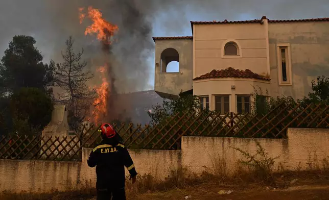 A volunteer firefighter observs a flame rising next to a house during a wildfire near Porto Germeno, northwest of Athens, Greece, Sunday, Aug. 2, 2026. (AP Photo/Michael Varaklas)