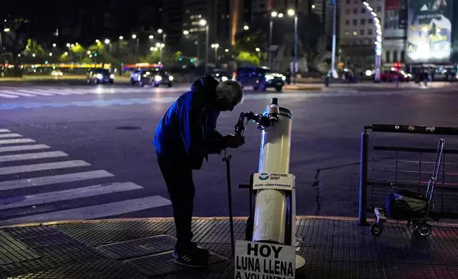 Juan Carlos Sanchez adjusts his telescope as he waits for customers to offer them a chance to view the moon in exchange for a voluntary contribution during a partial lunar eclipse in Buenos Aires, Argentina, Thursday, Aug. 27, 2026. (AP Photo/Natacha Pisarenko)