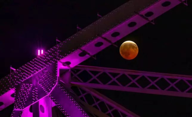 A partial lunar eclipse is seen by the purple lit steel beams of the Crescent City Connection, a pair of bridges that span the Mississippi River, in New Orleans, Thursday, Aug. 27, 2026. (AP Photo/Matthew Hinton)