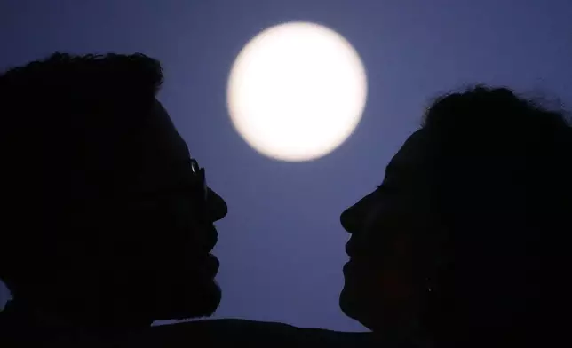 A couple embrace as the full moon rises hours before a lunar eclipse at the Santa Luzia viewpoint in Lisbon, Thursday, Aug. 27, 2026. (AP Photo/Armando Franca)