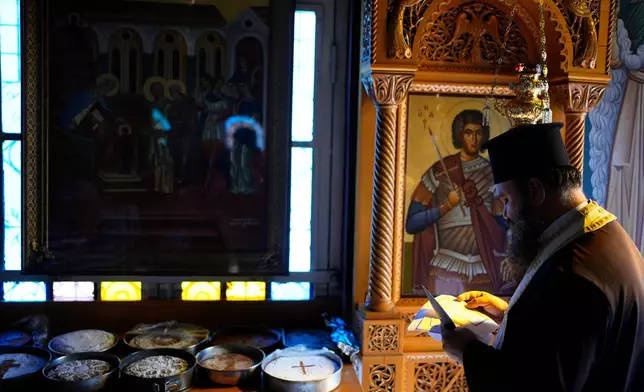 Father Nikolaos Vlavianos blesses the parishioners' Fanouropites, orange-flavored cakes, as an icon of Saint Fanourios, known in Greek as "The Revealer," is seen at right at the Church of St. Fanourios in Athens, Tuesday, Aug. 25, 2026. (AP Photo/Thanassis Stavrakis)