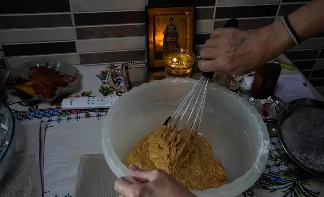 Maria Chanioti, 66, prepares Fanouropita, an orange-flavored cake, as a small icon of Saint Fanourios, known in Greek as "The Revealer," is seen in the background in Athens, Wednesday, Aug. 26, 2026. (AP Photo/Thanassis Stavrakis)