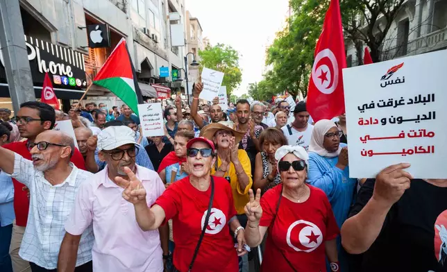 People take part in a protest against rising prices, declining purchasing power and shortages of basic goods in Tunis, Tunisia, Thursday, Aug. 20, 2026. Banner in Arabic reads "The country is drowning in debt". (AP Photo/Ons Abid)