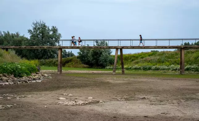 People walk across a footbridge over a dry river bed near Beusichem, Netherlands, Thursday, July 30, 2026, during drought conditions. (AP Photo/Patrick Post)