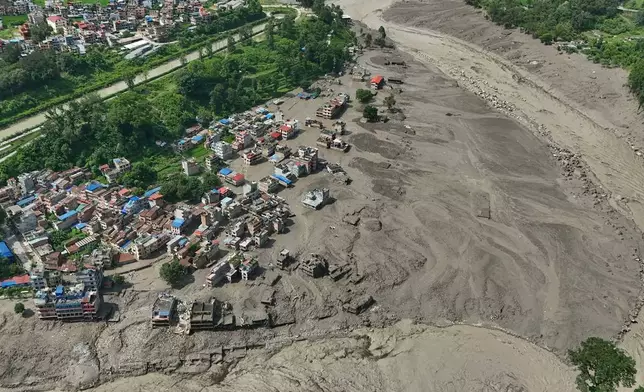 Damaged houses stand precariously near the swollen, debris-choked banks of the Trishuli River after flash floods in Nepal's Nuwakot district on Wednesday, Aug. 26, 2026. (AP Photo/Niranjan Shrestha)