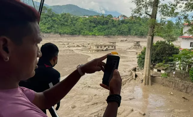 People take photographs and videos of the swollen, debris-choked banks of the Trishuli River after a flash floods in Nepal's Nuwakot district on Wednesday, Aug. 26, 2026. (AP Photo/Niranjan Shrestha)