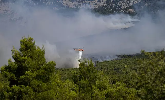 A firefighting helicopter drops water over a smoke-filled forest during a wildfire near Porto Germeno, northwest of Athens, Greece, Sunday, Aug. 2, 2026. (AP Photo/Michael Varaklas)