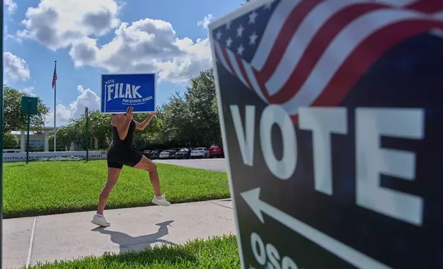 Yvette Allen, of Celebration, Fla., exercises while holding up a sign for a local school board election outside of the West Osceola Branch Library, during early voting for the Florida primary election, in Celebration, Fla., Thursday, Aug. 13, 2026. (AP Photo/Jacquelyn Martin)
