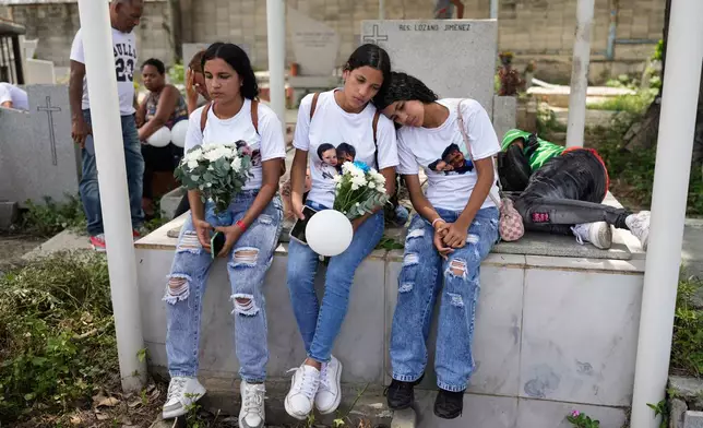 Noemi Marrero, left, and her sisters sit at a cemetery in La Guaira, Venezuela, during the funeral of Marrero's two children, who died in the earthquakes, Monday, Aug. 17, 2026. (AP Photo/Ariana Cubillos)