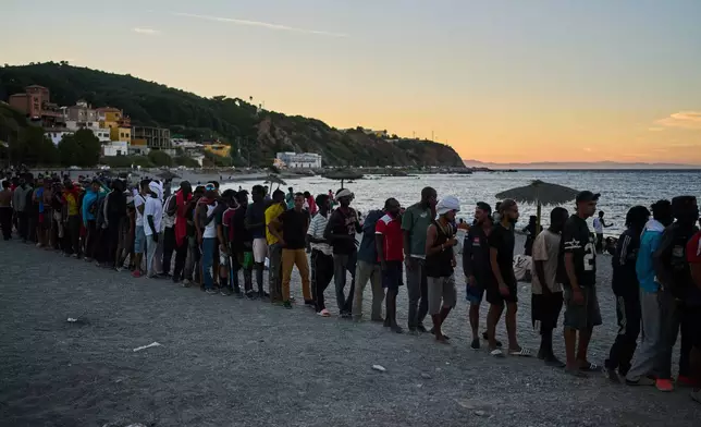 Migrants who crossed from Morocco into Spain line up for food distribution on a beach in the Spanish enclave of Ceuta, Monday, Aug. 3, 2026. (AP Photo/Bernat Armangue)