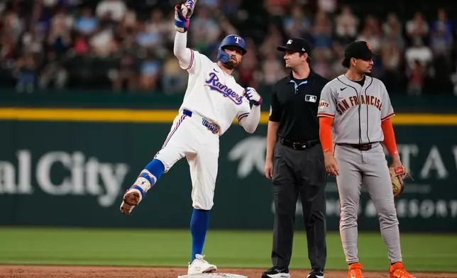 Texas Rangers' Brandon Nimmo, left, celebrates his run-scoring double in front of umpire Adam Beck and San Francisco Giants shortstop Willy Adames, right, in the first inning a baseball game in Arlington, Texas, Tuesday, Aug. 4, 2026. (AP Photo/Tony Gutierrez)