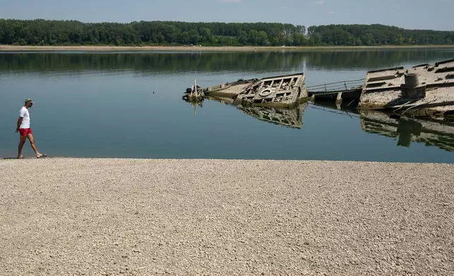 A man walks on the sandbank by the wreckage of a WWII German warship, emerged due to the drought, in front of Djerdap II, a large dam on the Danube River, between Romania and Serbia, near Prahovo, Serbia, Tuesday, Aug. 4, 2026. (AP Photo/Darko Vojinovic)