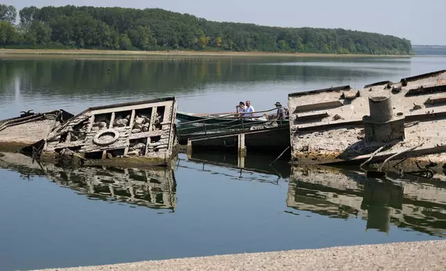 People watch the wreckage of a WWII German warship, emerged due to the drought, in front of Djerdap II, a large dam on the Danube River, between Romania and Serbia, near Prahovo, Serbia, Tuesday, Aug. 4, 2026. (AP Photo/Darko Vojinovic)