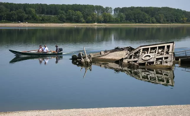 People watch the wreckage of a WWII German warship, emerged due to the drought, in front of Djerdap II, a large dam on the Danube River, between Romania and Serbia, near Prahovo, Serbia, Tuesday, Aug. 4, 2026. (AP Photo/Darko Vojinovic)