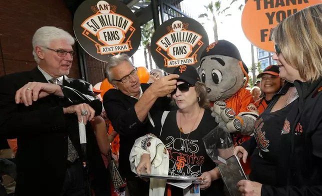 FILE - San Francisco Giants fan Grace Witt, center, is given a hat and jersey by announcers Mike Krukow, left, and Duane Kuiper after she was announced at the 50 millionth fan at AT&T Park, before a baseball game between the Giants and the Philadelphia Phillies in San Francisco, July 11, 2015. (AP Photo/Jeff Chiu, File)