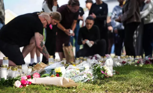 People leave flowers and candles at a makeshift memorial outside a school in Fagersta, Sweden, Saturday Aug. 22, 2026, the day after an 18-year-old with a sword attacked the school killing one person and seriously injuring two others. (Magnus Lejhall/TT via AP)
