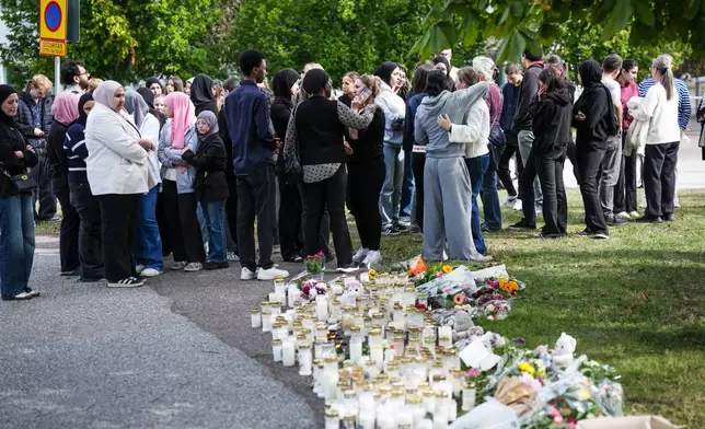 People leave flowers and candles at a makeshift memorial outside a school in Fagersta, Sweden, Saturday Aug. 22, 2026, the day after an 18-year-old with a sword attacked the school killing one person and seriously injuring two others. (Magnus Lejhall/TT via AP)