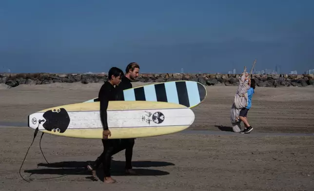 Researcher Michael McNamara carries a beach seine to catch stingrays as he walks past surfers in Seal Beach, Calif., Friday, Aug. 7, 2026. (AP Photo/Jae C. Hong)