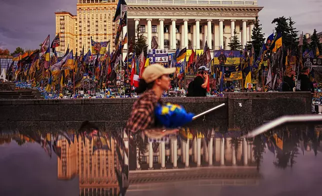 The National Music Academy, right, is reflected on a metro entrance at Independence square where Ukrainian flags and photographs are placed in memory of civilians and soldiers killed during the war with Russia, in central Kyiv, Tuesday, Aug. 18, 2026. (AP Photo/Francisco Seco)
