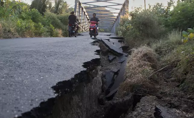 Motorists ride their motorbikes near an earthquake-damaged road in North Lamba Leda, East Nusa Tenggara province, Indonesia, Tuesday, Aug. 18, 2026. (AP Photo/Firdia Lisnawati)