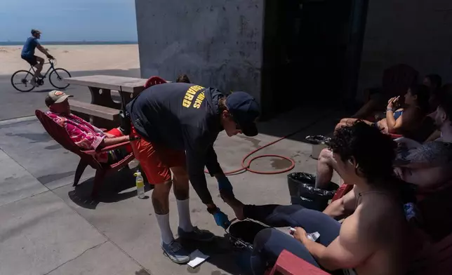 Lifeguard Max Voci, center, treats beachgoers for stingray stings at Bolsa Chica State Beach in Huntington Beach, Calif., Friday, July 24, 2026. (AP Photo/Jae C. Hong)