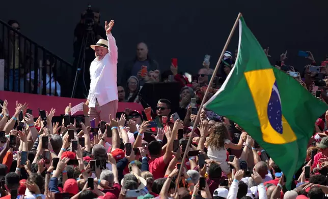 Brazilian President Luiz Inacio Lula da Silva waves to supporters as a Brazilian flag is held nearby during a presidential election campaign rally in Sao Bernardo do Campo, Sao Paulo state, Brazil, Sunday, Aug. 16, 2026. (AP Photo/Andre Penner)