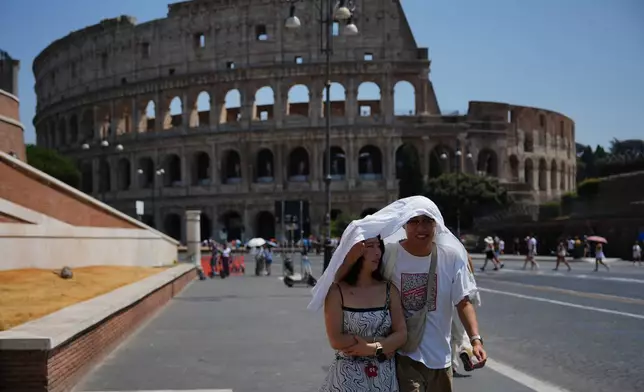 Tourists take shelter as they walk in front of the Rome'a ancient Colosseum, Saturday, Aug. 1, 2026. (AP Photo/Alessandra Tarantino)